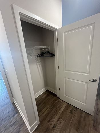 A white door is open to a closet with clothes hanging inside.